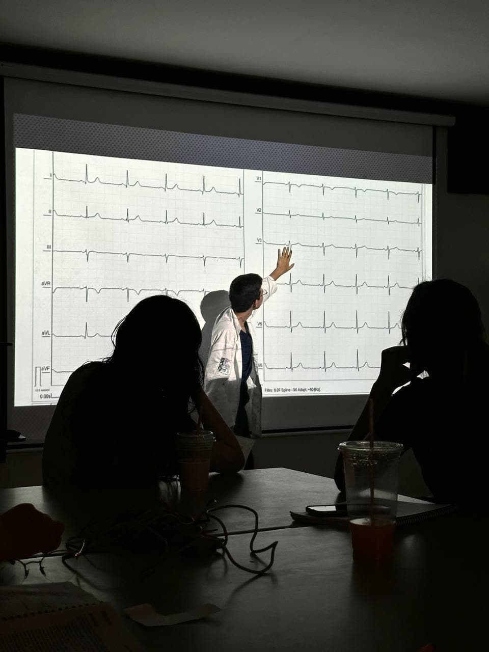 Asesor de GALEA señalando un electrocardiograma de doce derivaciones proyectado, con alumnos siguiendo la clase